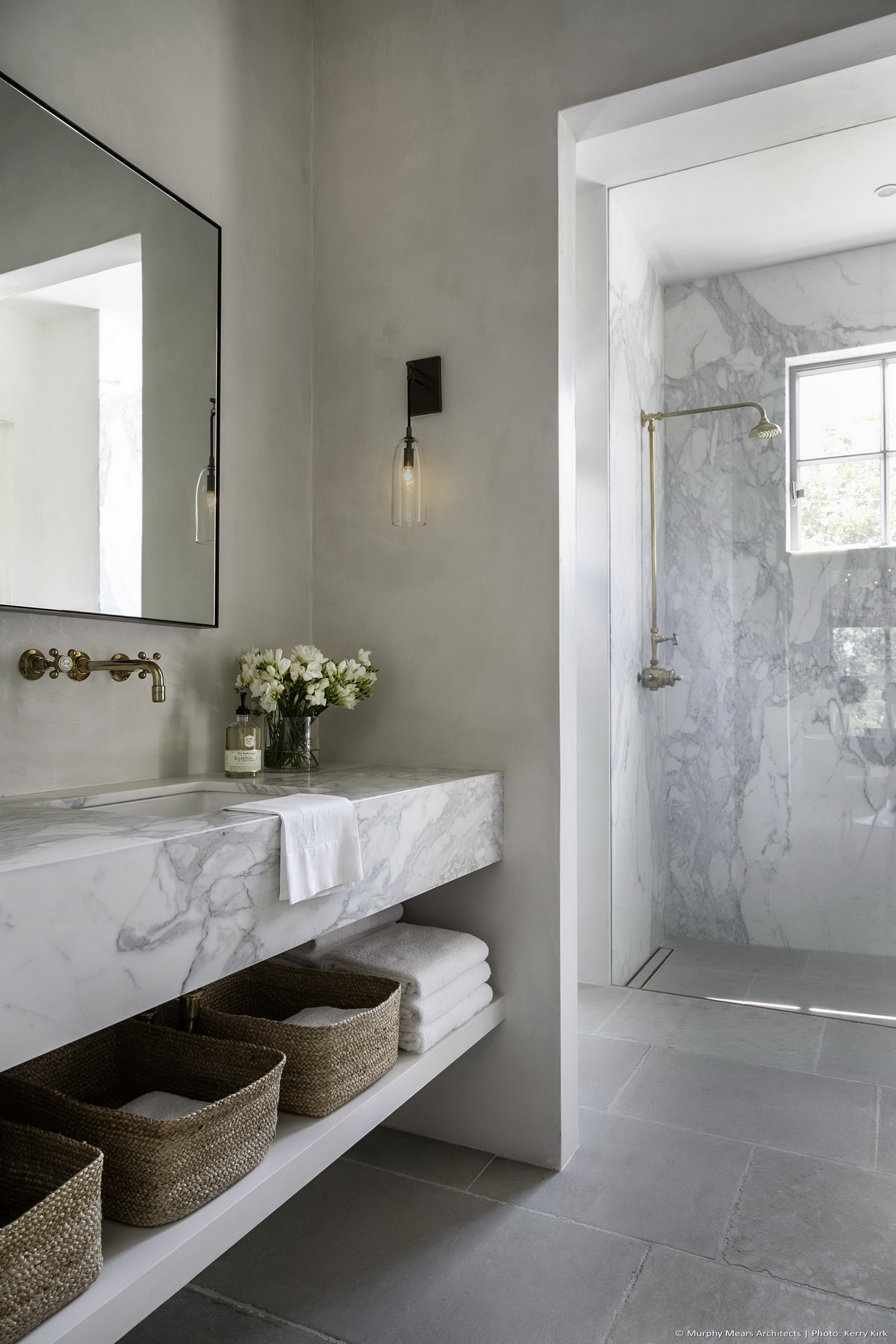 Guest bath with marble sink, plaster walls, limestone floors, and a marble shower beyond.
